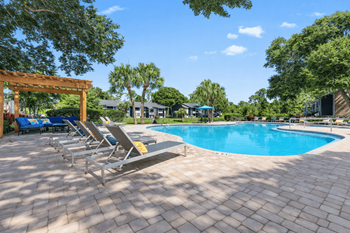 A pool surrounded by trees and chairs.